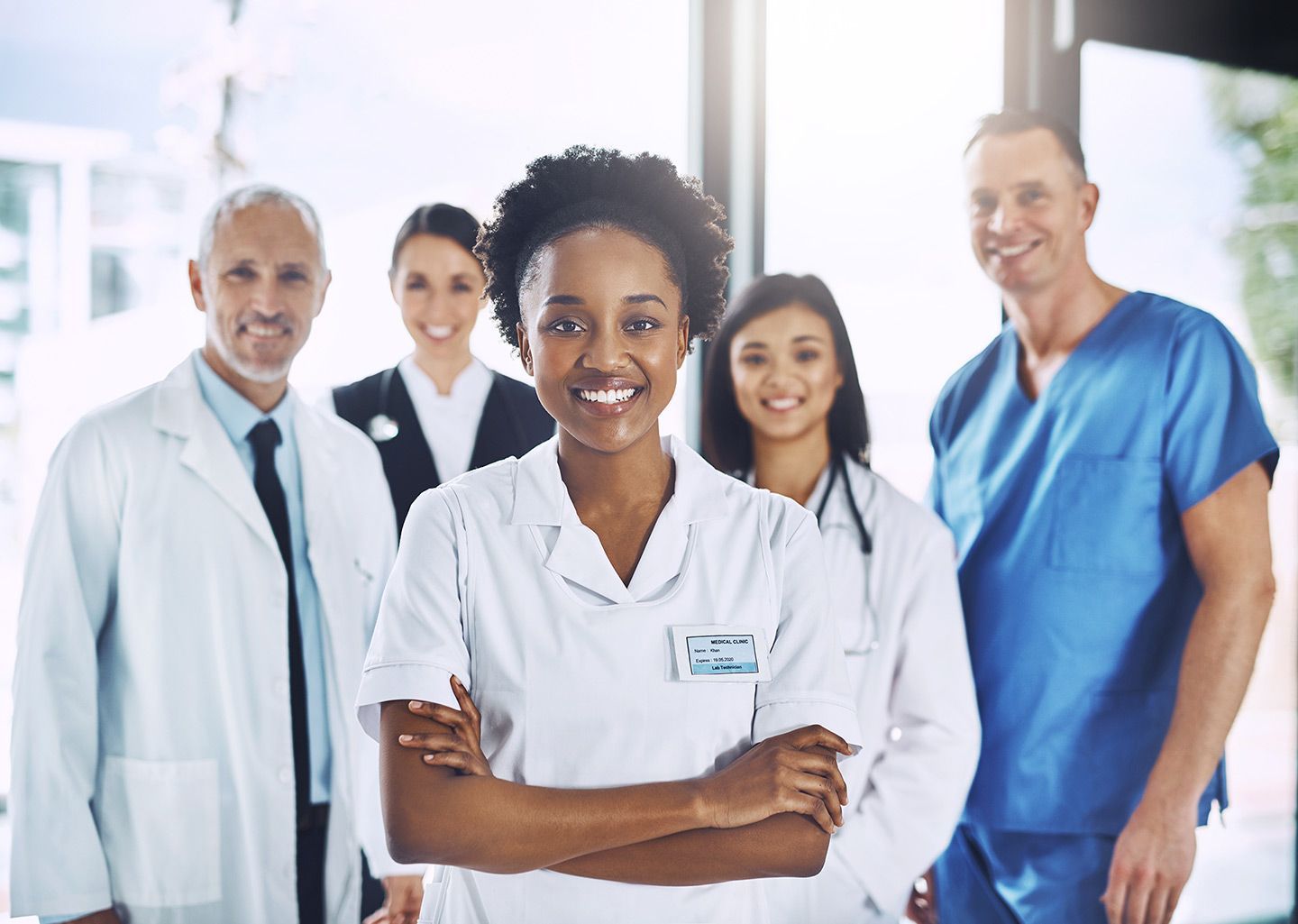 Medical team smiling, arms crossed. Wearing white coats and scrubs in a bright room.