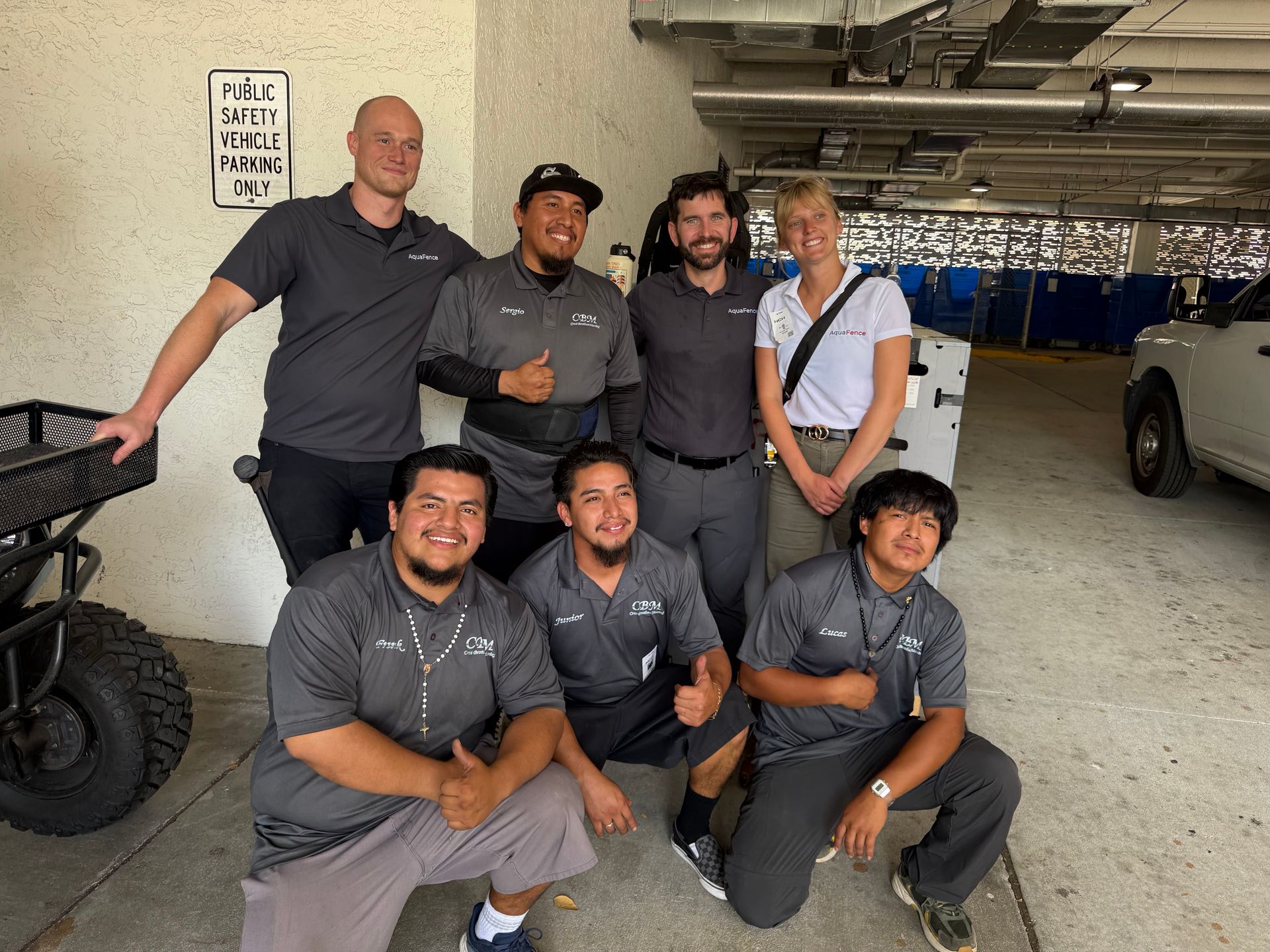 Group of seven people posing in a parking garage, smiling in matching gray shirts