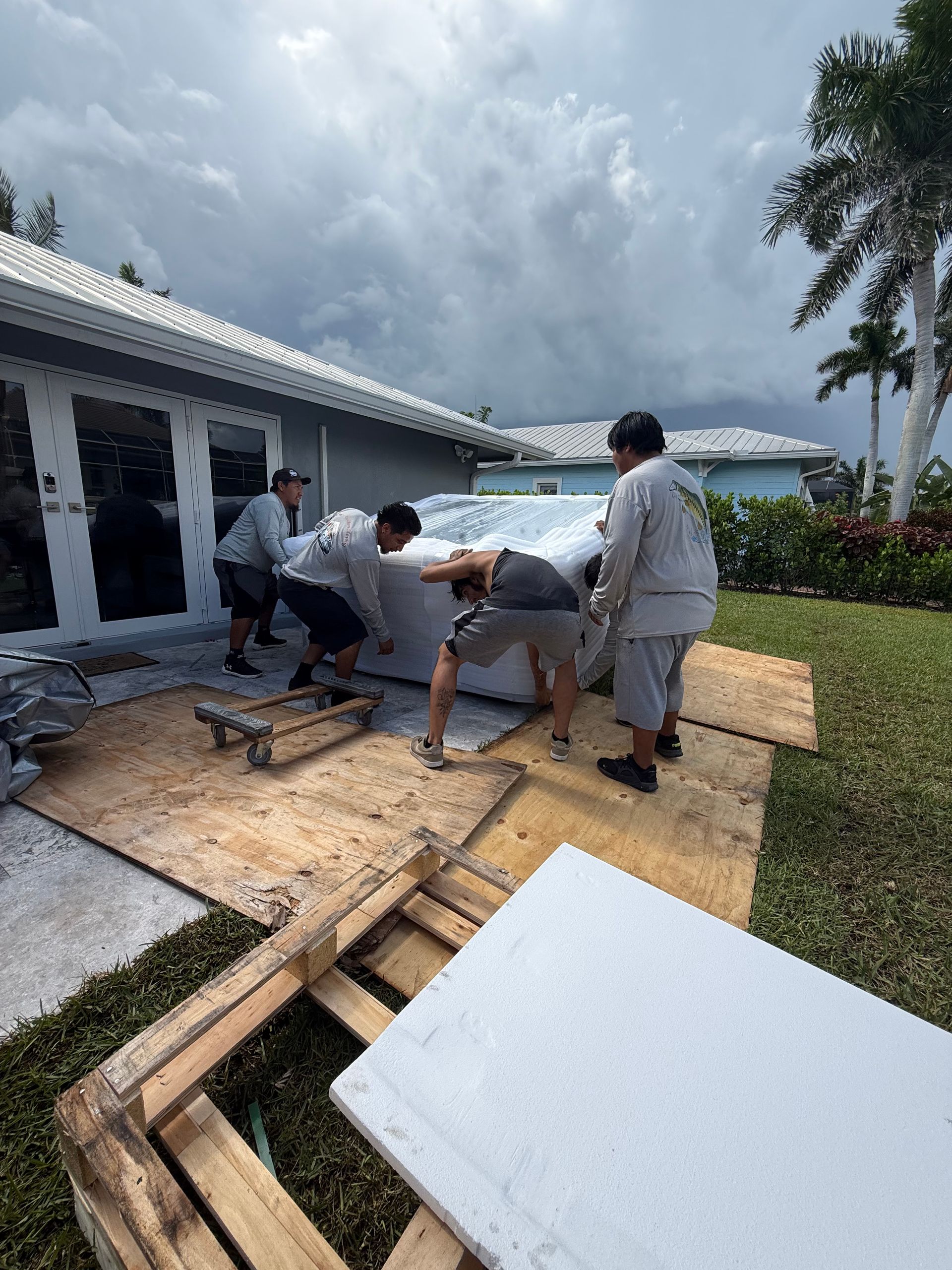 Workers lifting a large white panel beside a house under cloudy skies