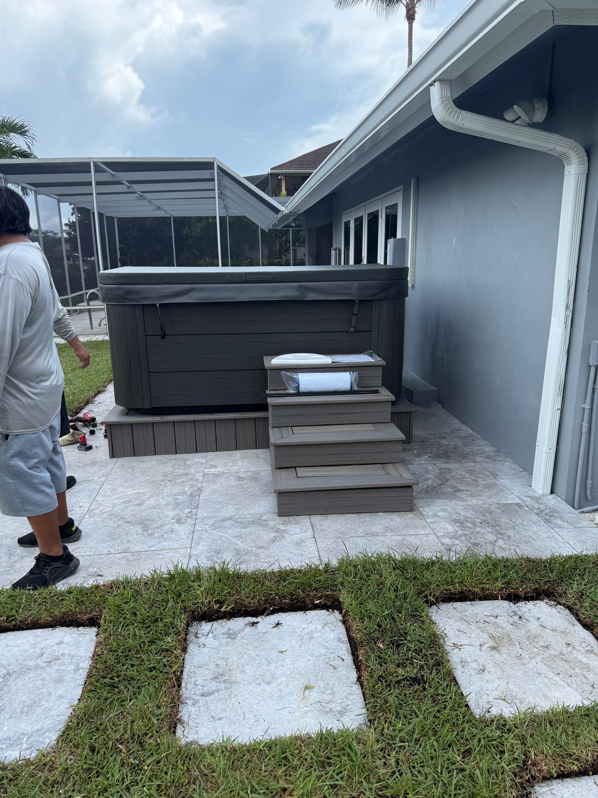 Backyard with gray hot tub, small wooden steps, and white gravel beside a house