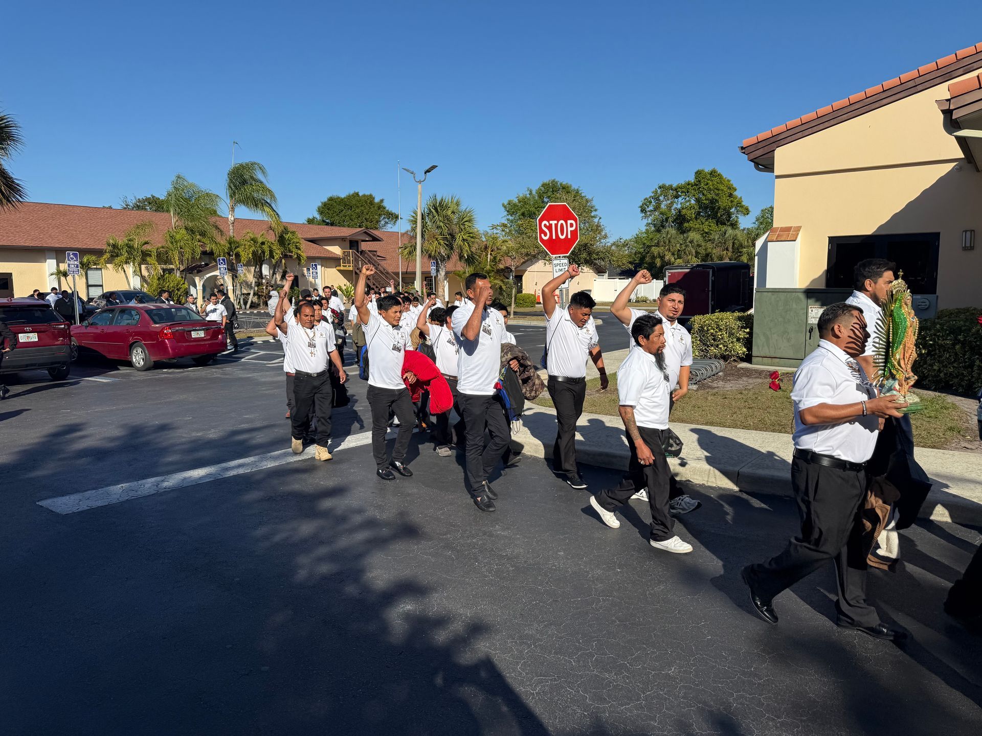 People marching in a neighborhood street with stop sign and houses in the background.