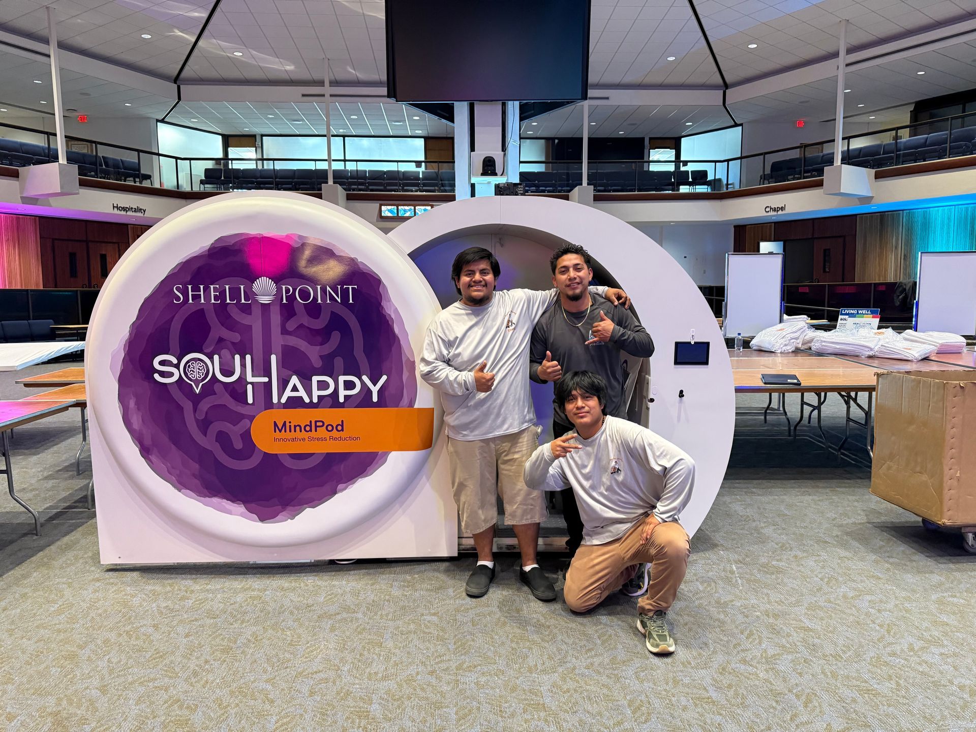 Three people posing in front of a “Soul Happy” event sign in a bright indoor venue