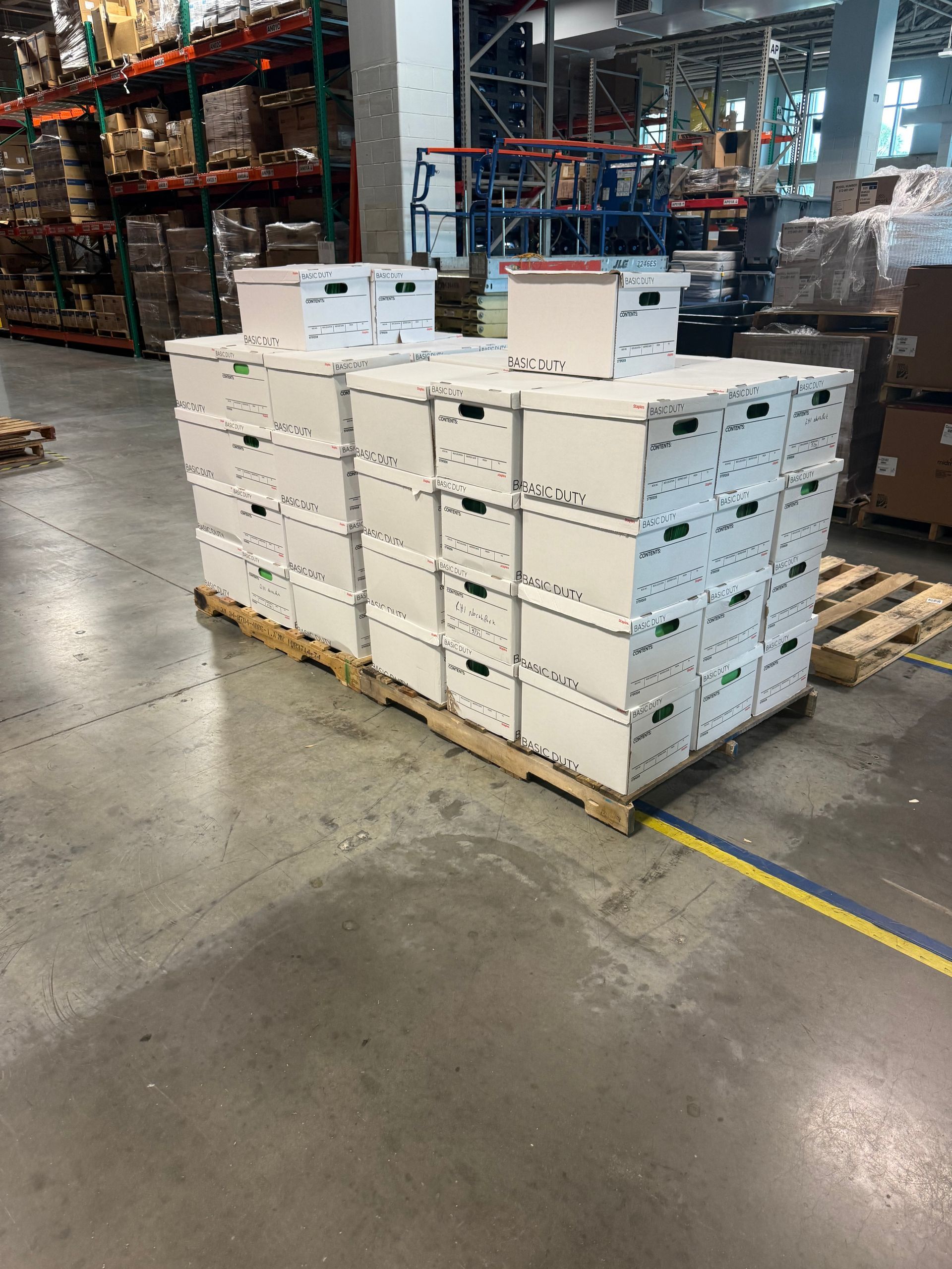 Stacked white boxes on a pallet in a warehouse aisle