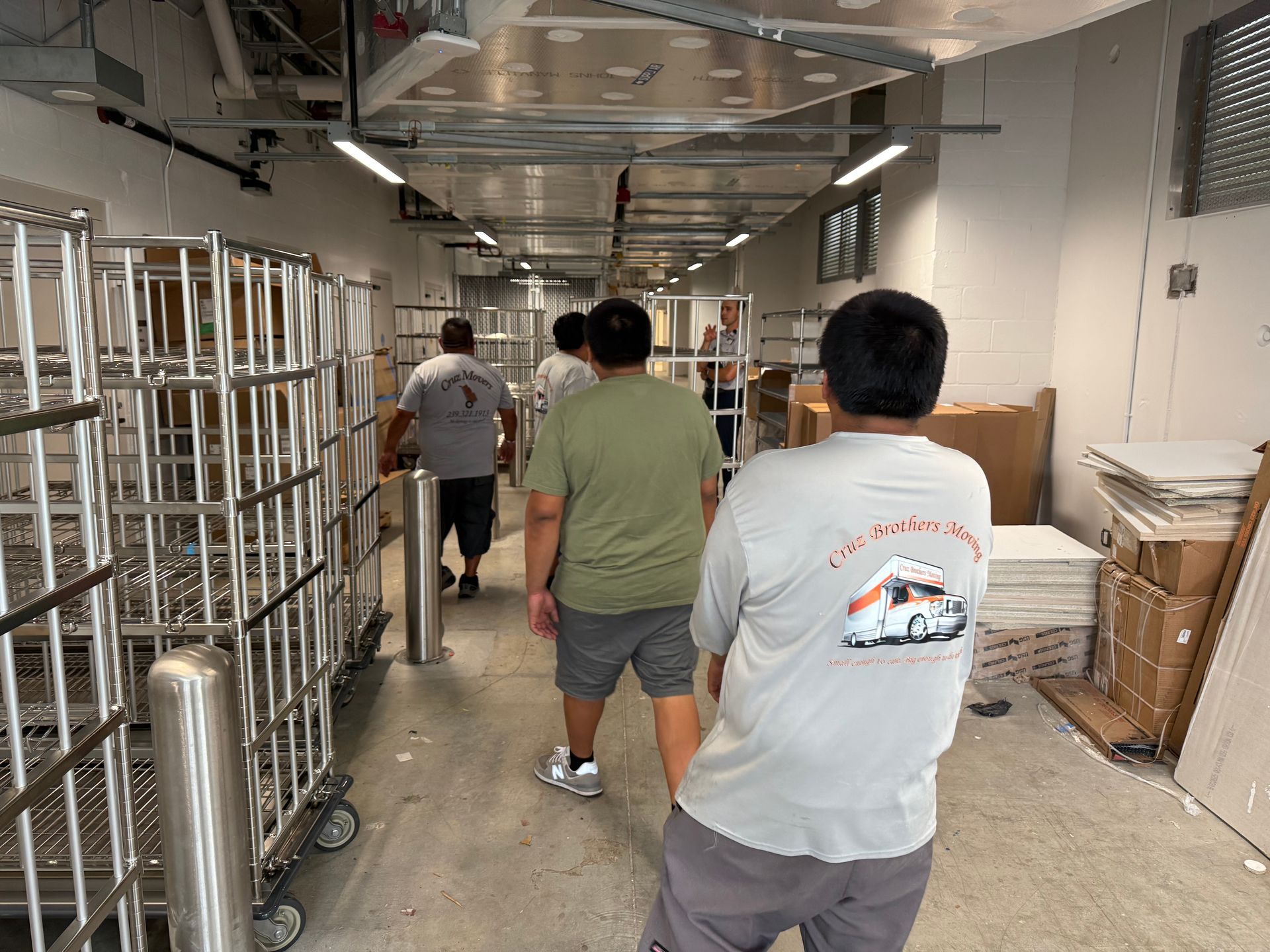 People walking through a warehouse hallway with metal racks and stacked boxes