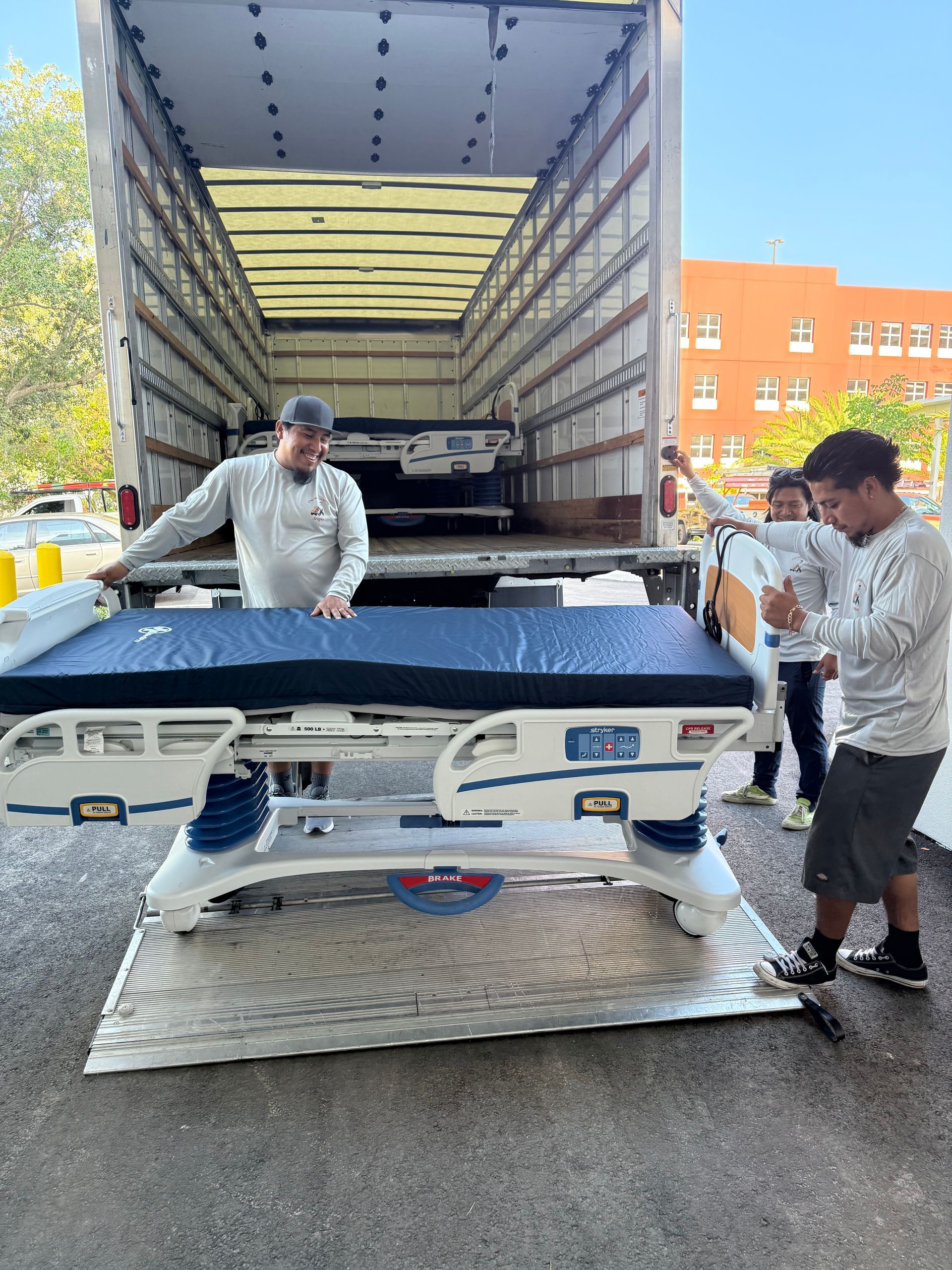 Two people loading a damaged blue car into a shipping container in a parking lot.