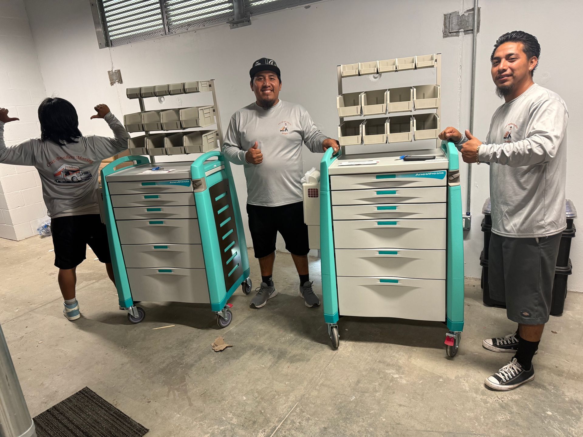 Three workers in a warehouse stand beside teal rolling tool carts with drawers.