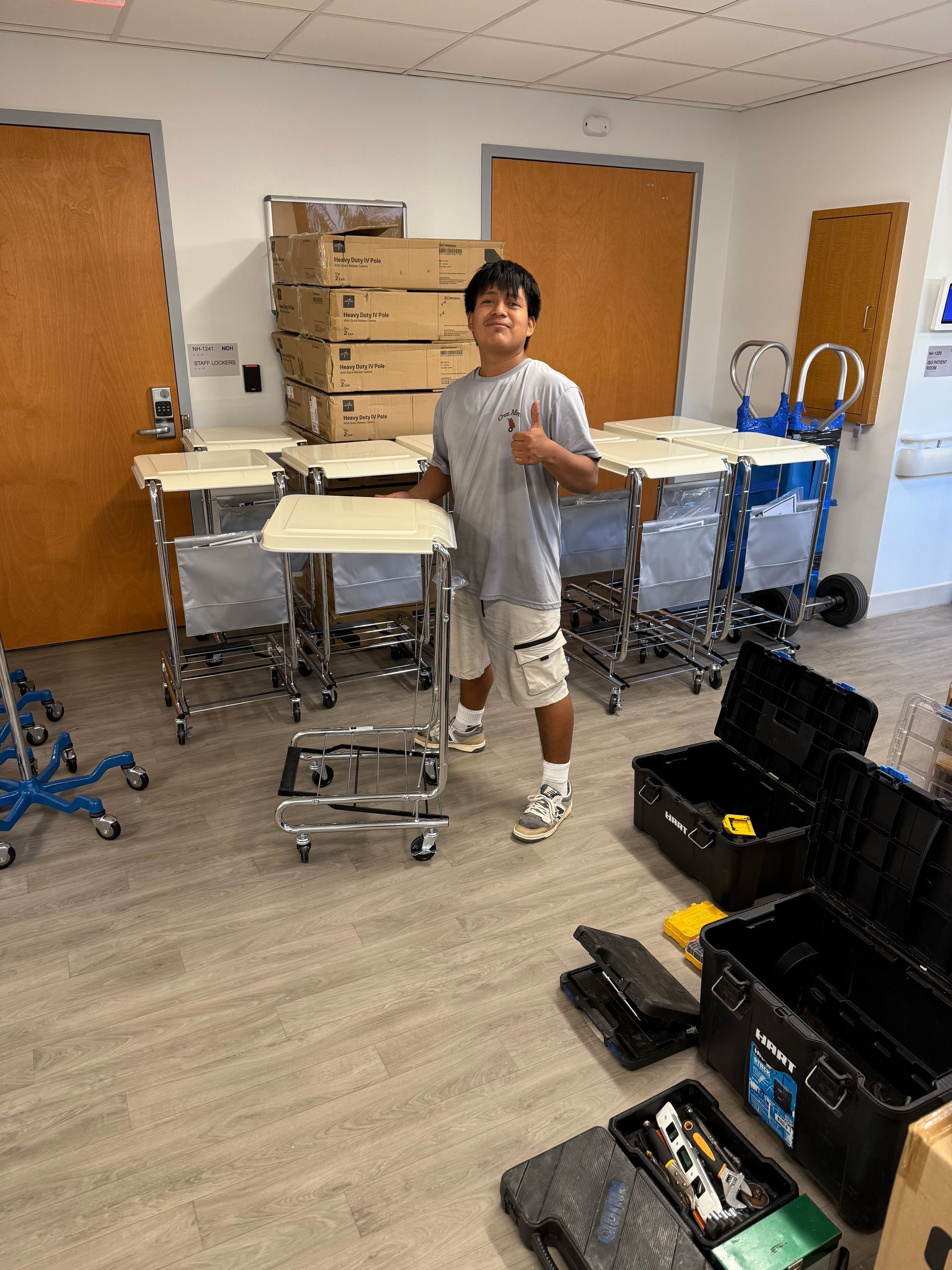 Person standing in a storage room with stacked boxes, tables, and equipment cases.