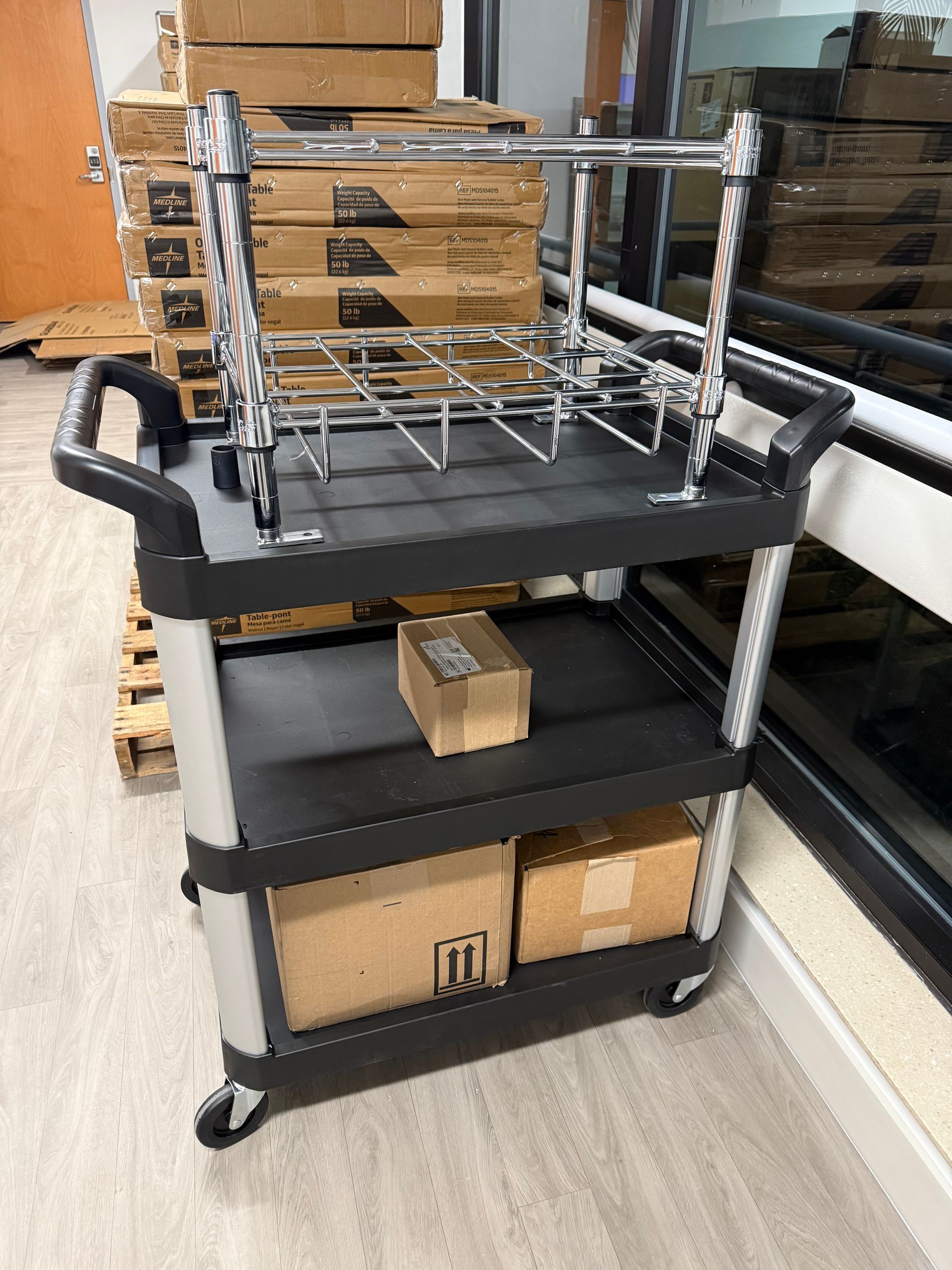 Black rolling cart with shelves and wire rack, loaded with cardboard boxes in a warehouse corridor