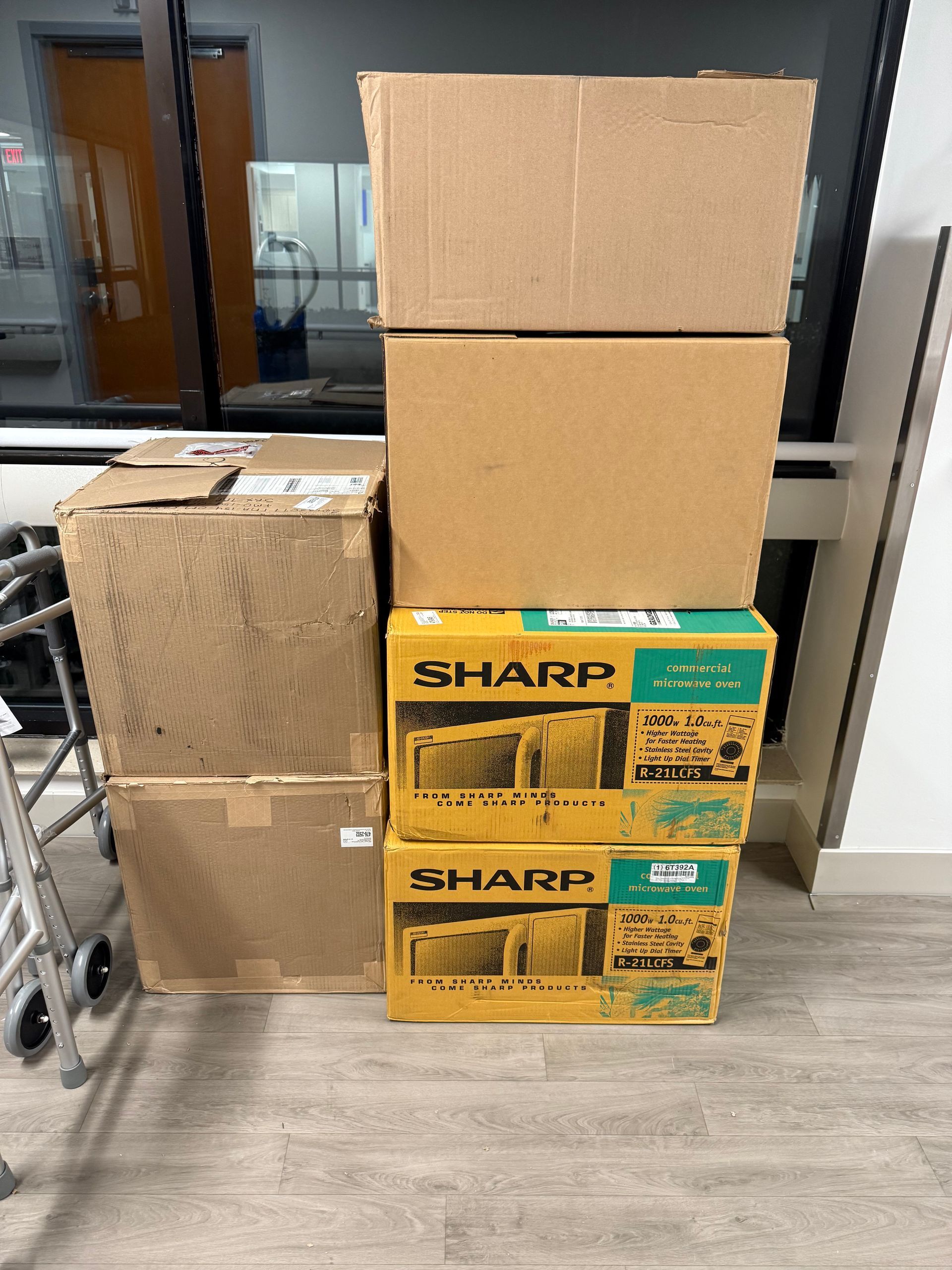 Stacked cardboard boxes and Sharp appliance cartons in a hallway near glass doors