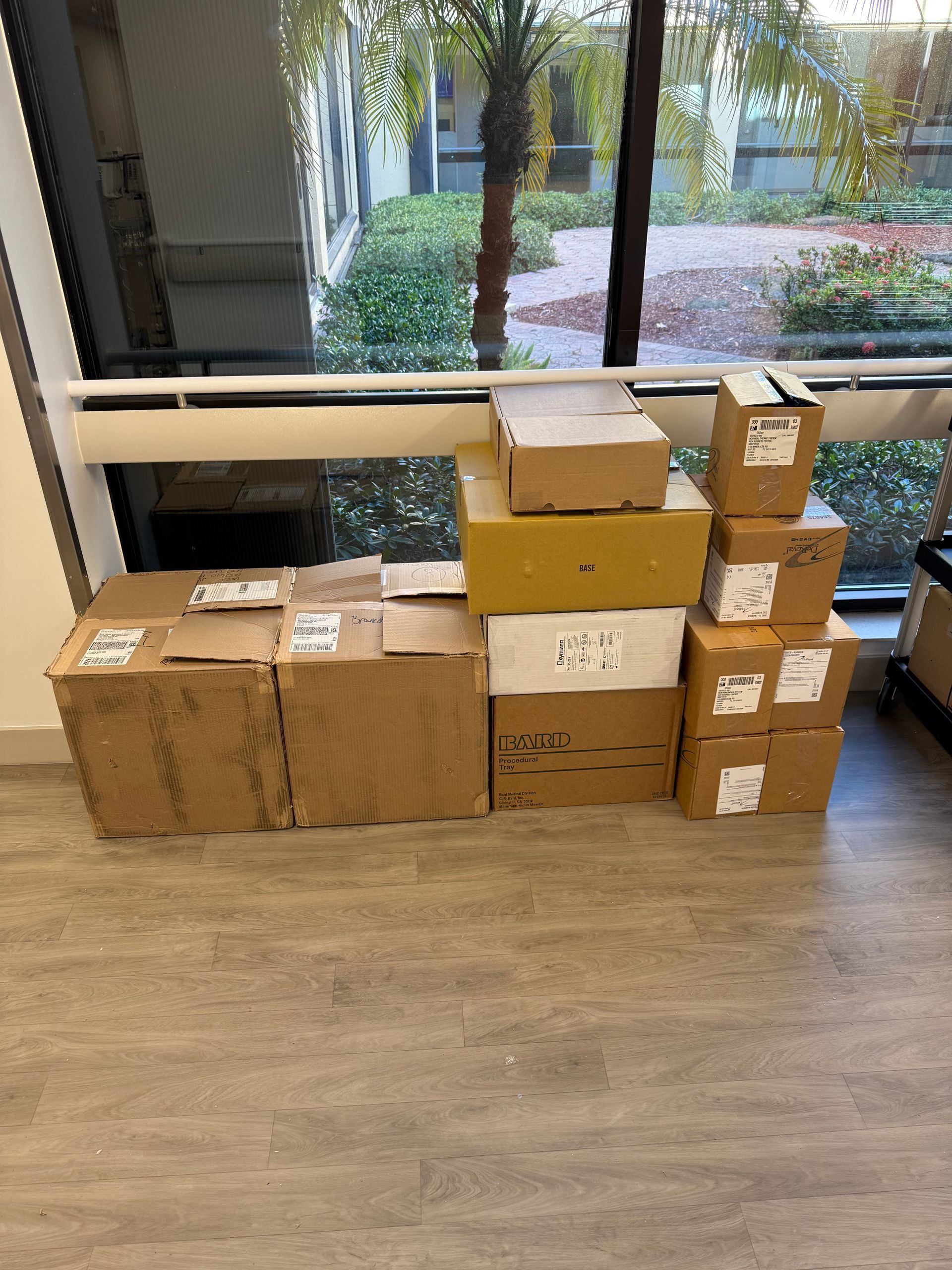 Stacked cardboard boxes by a window on a wooden floor in an office or lobby