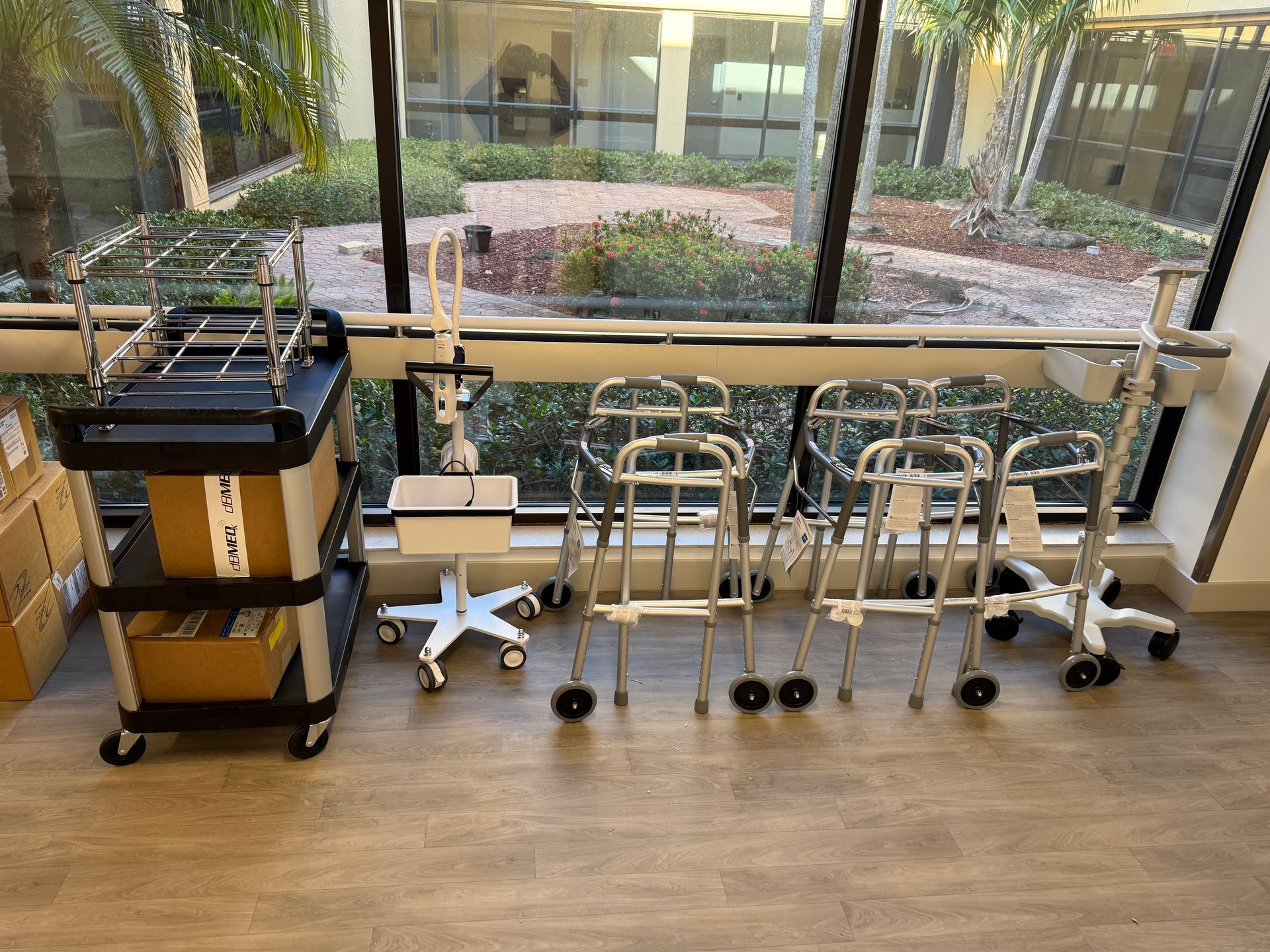 Hospital corridor with walkers and a cart lined up beside a large window