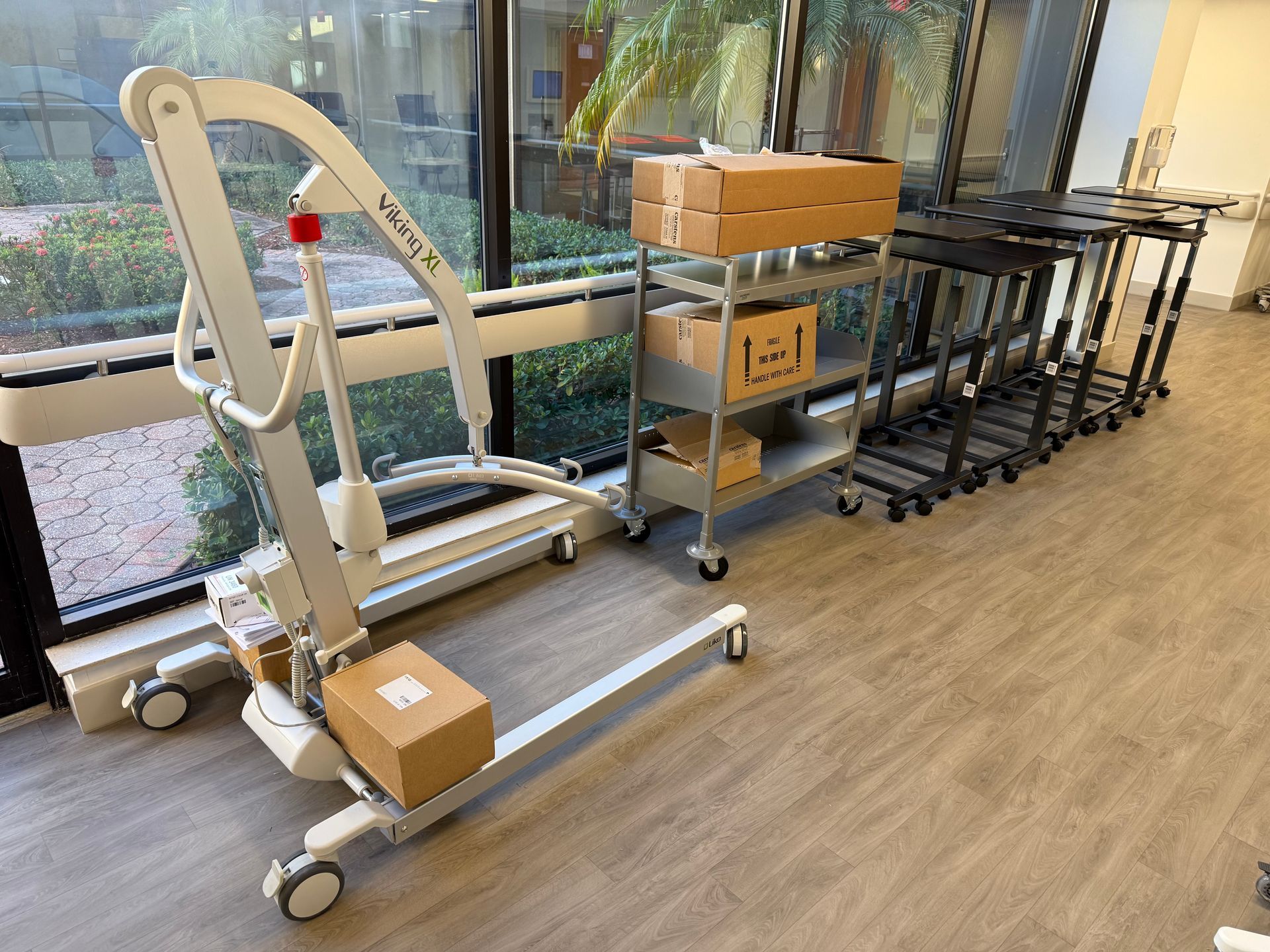 Hospital lift and wheeled cart in a bright hallway beside stacked boxes and folded carts