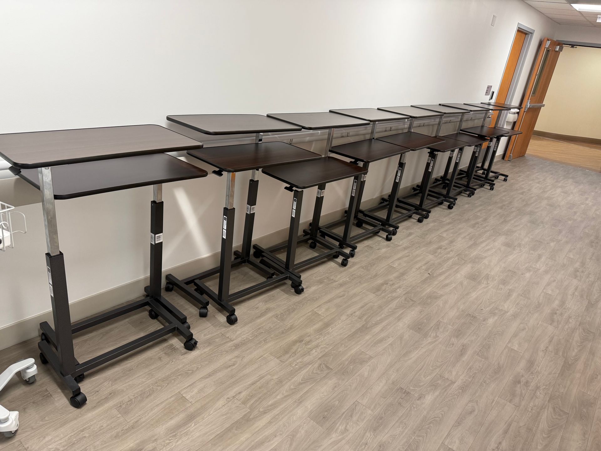 Row of adjustable standing desks lined along a wall in a bright office room