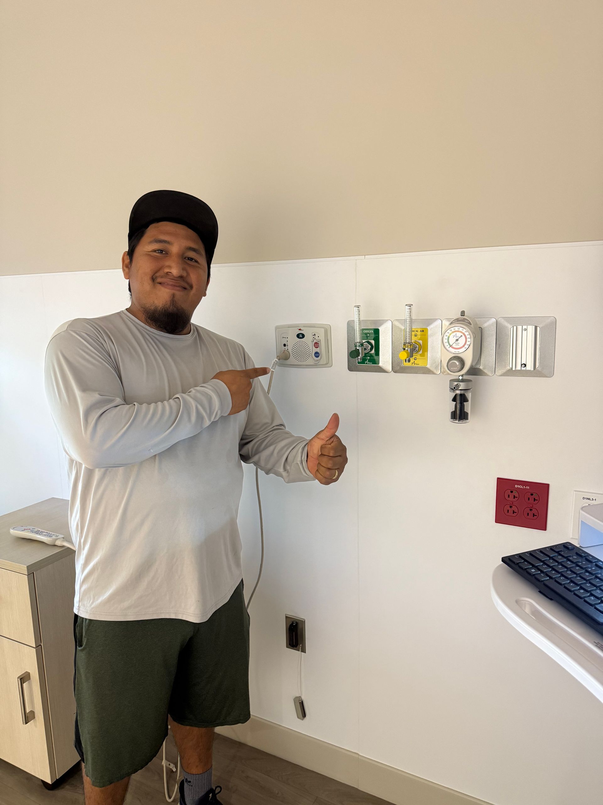 Person in a gray shirt and green shorts points at wall-mounted controls in a bright room.
