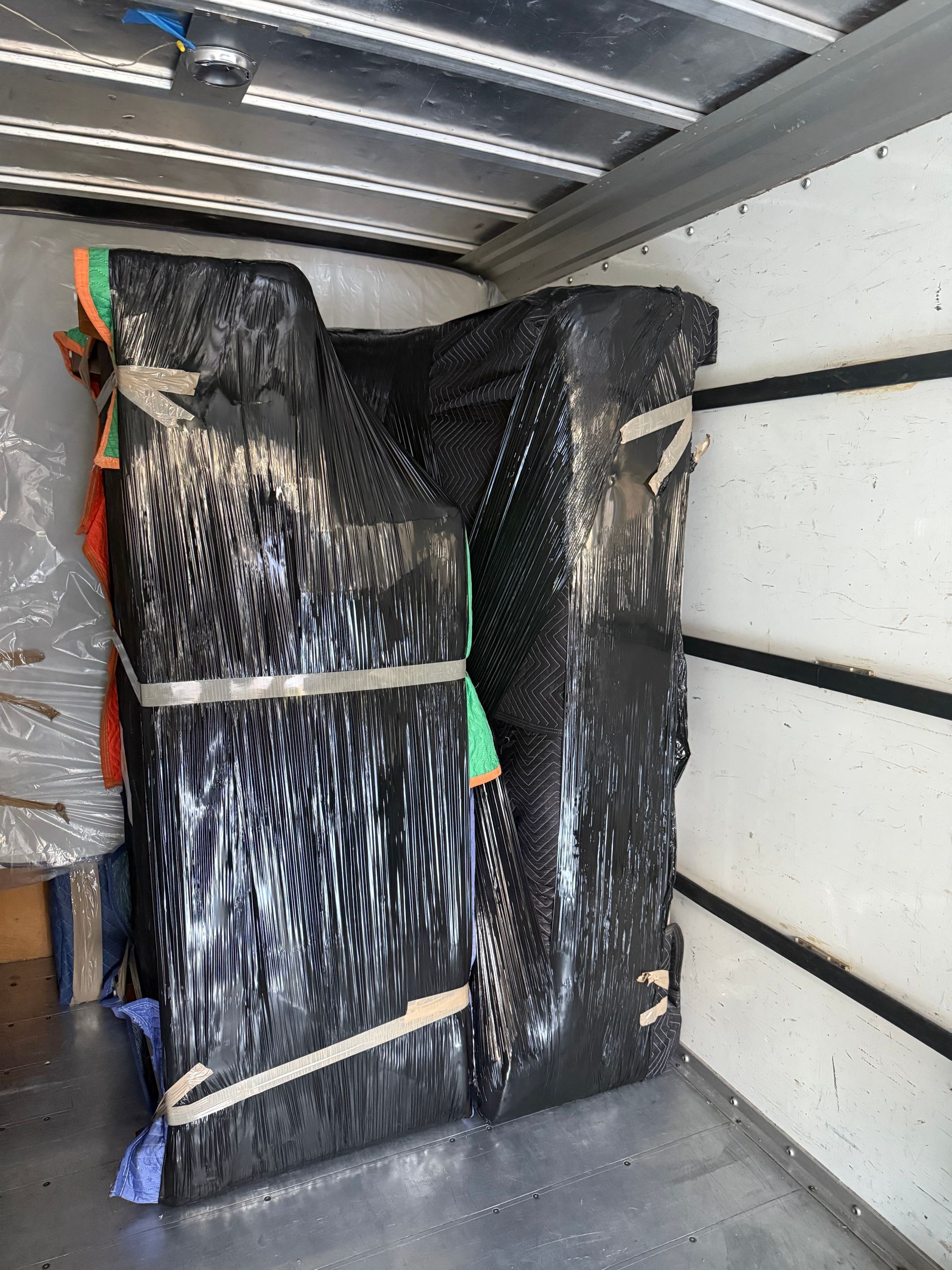 Packed black-wrapped furniture strapped inside a moving truck