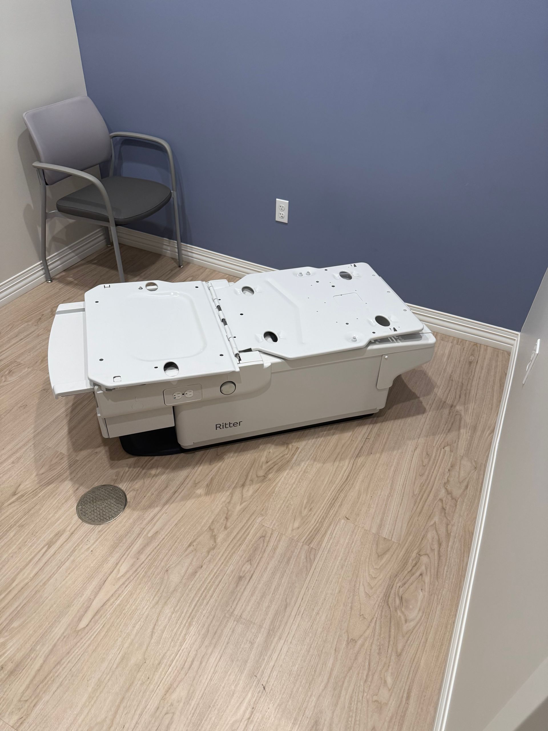 Hospital room with a bed or stretcher and a chair against a blue wall.