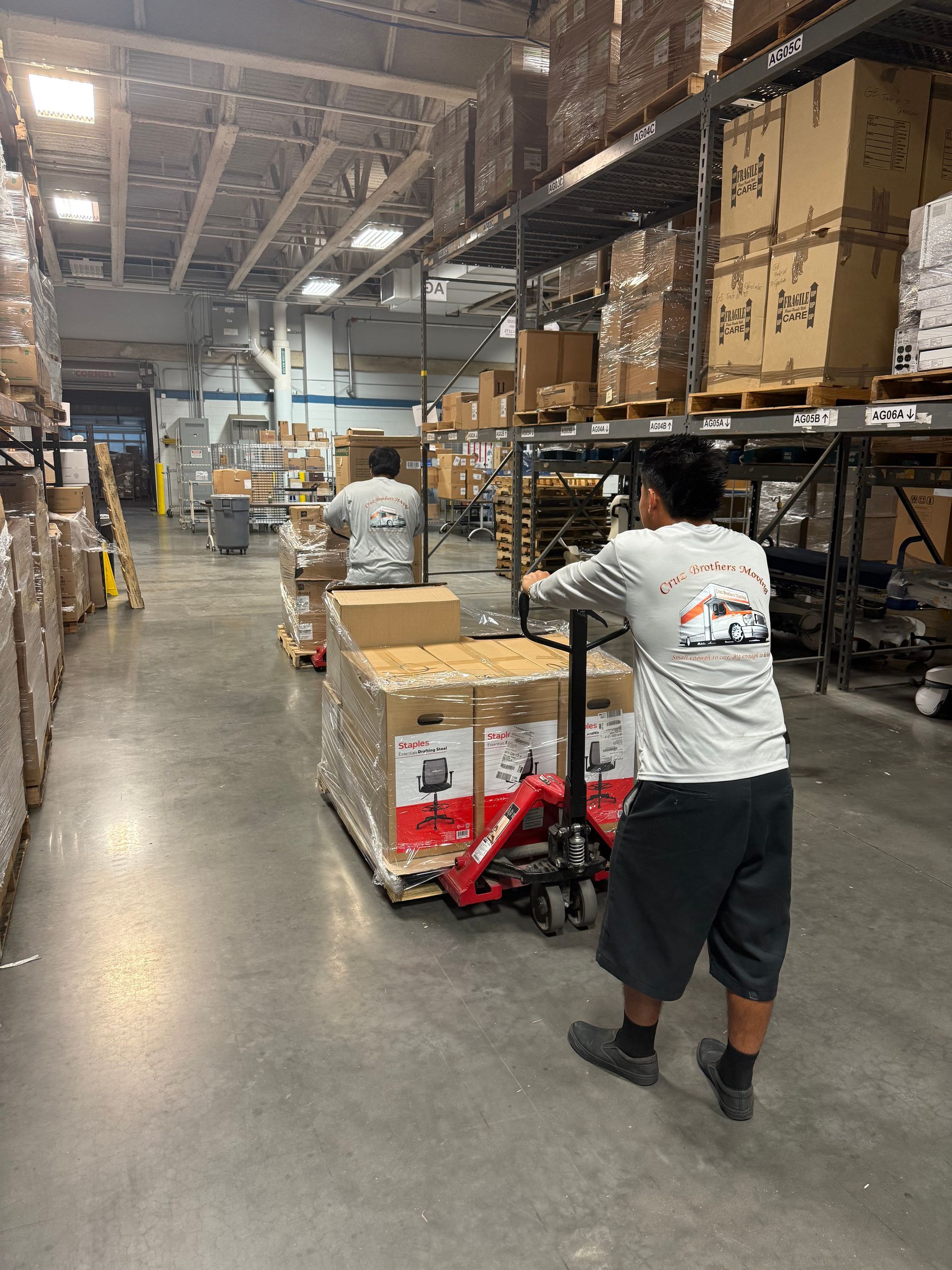 Workers moving boxes on carts through a warehouse aisle with tall shelving