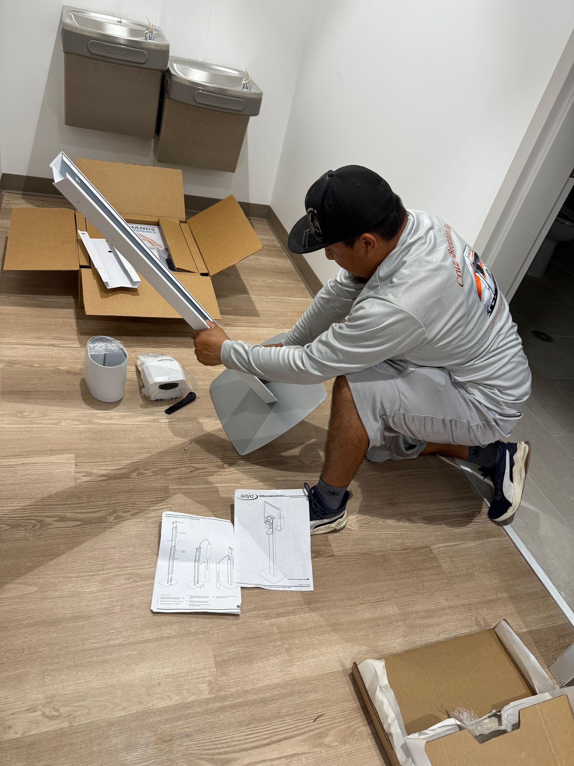 Person kneeling on a floor assembling cardboard packaging beside instruction sheets and shipping materials