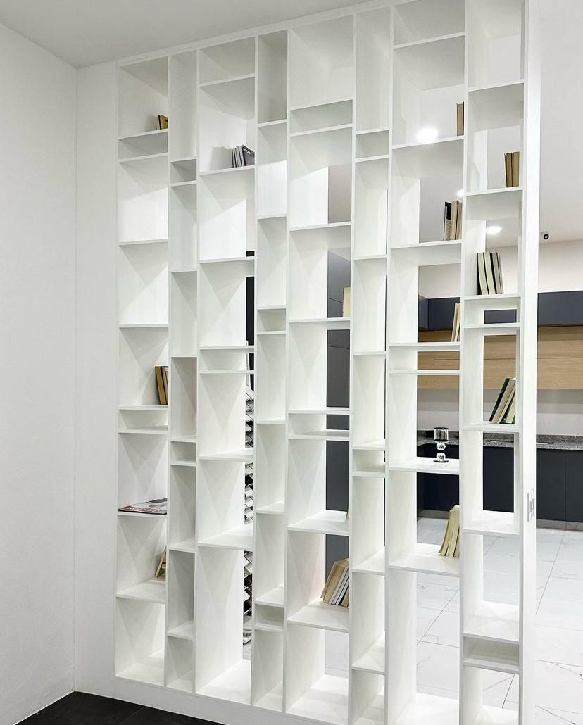 Estantería abierta de color blanco que divide una estancia y contiene objetos decorativos.