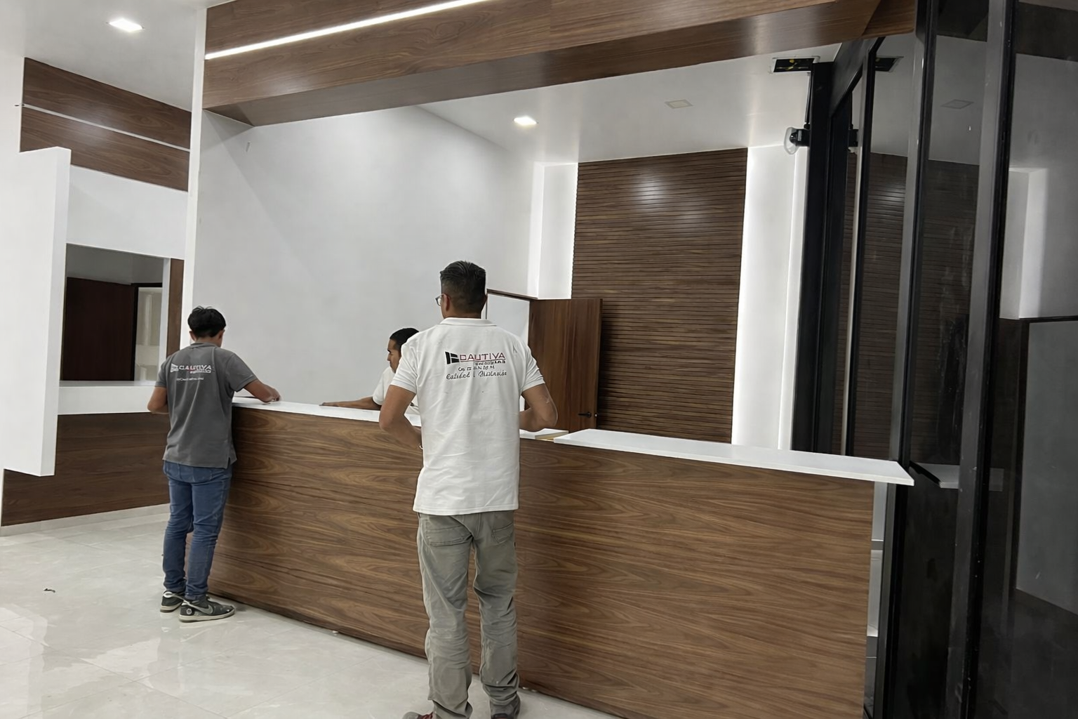 Tres personas instalando un mostrador de recepción de madera en un interior moderno.