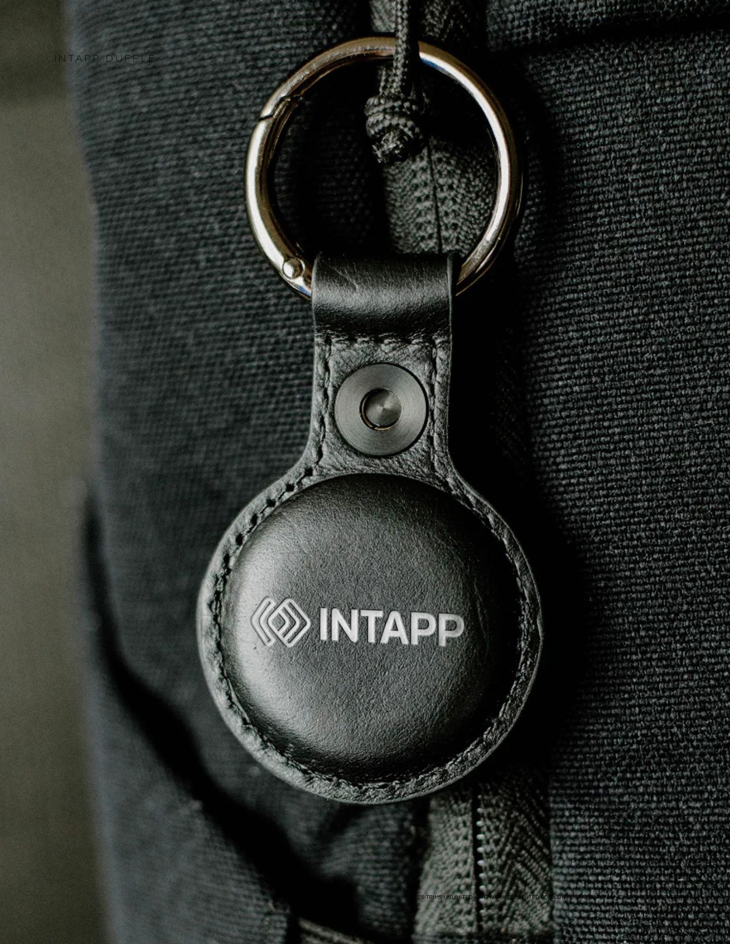 Black Intapp-branded tracking airtag attached to a keyring on a dark fabric surface.