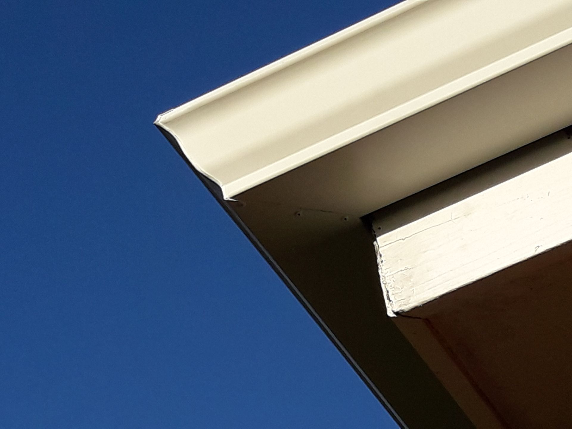 Close-up of a house roof with dark tiles, white soffit, and gutter against a blue sky
