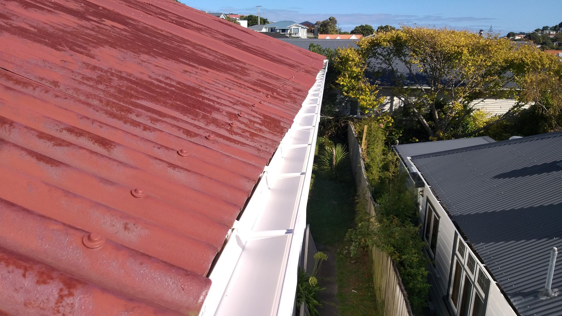 Red tiled roof with white gutters and a brown downspout on a house garage.