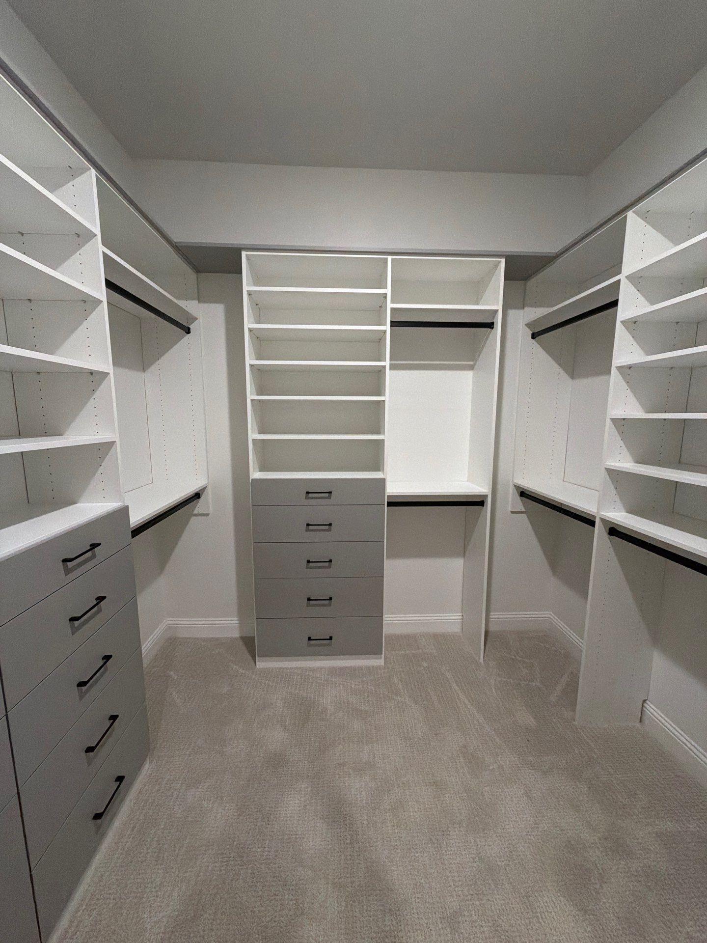 Empty walk-in closet with white shelves and gray drawers on beige carpet