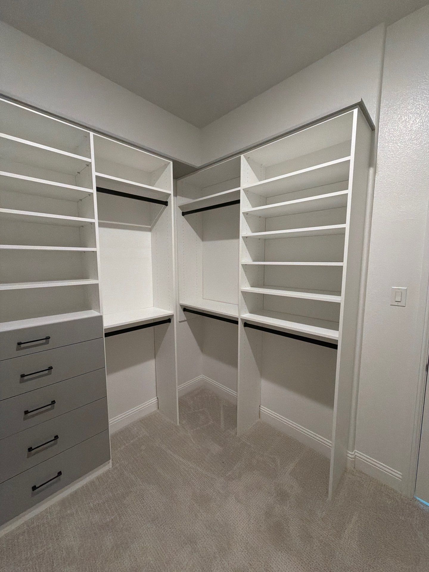 Empty walk-in closet with white built-in shelves, drawers, and beige carpet.
