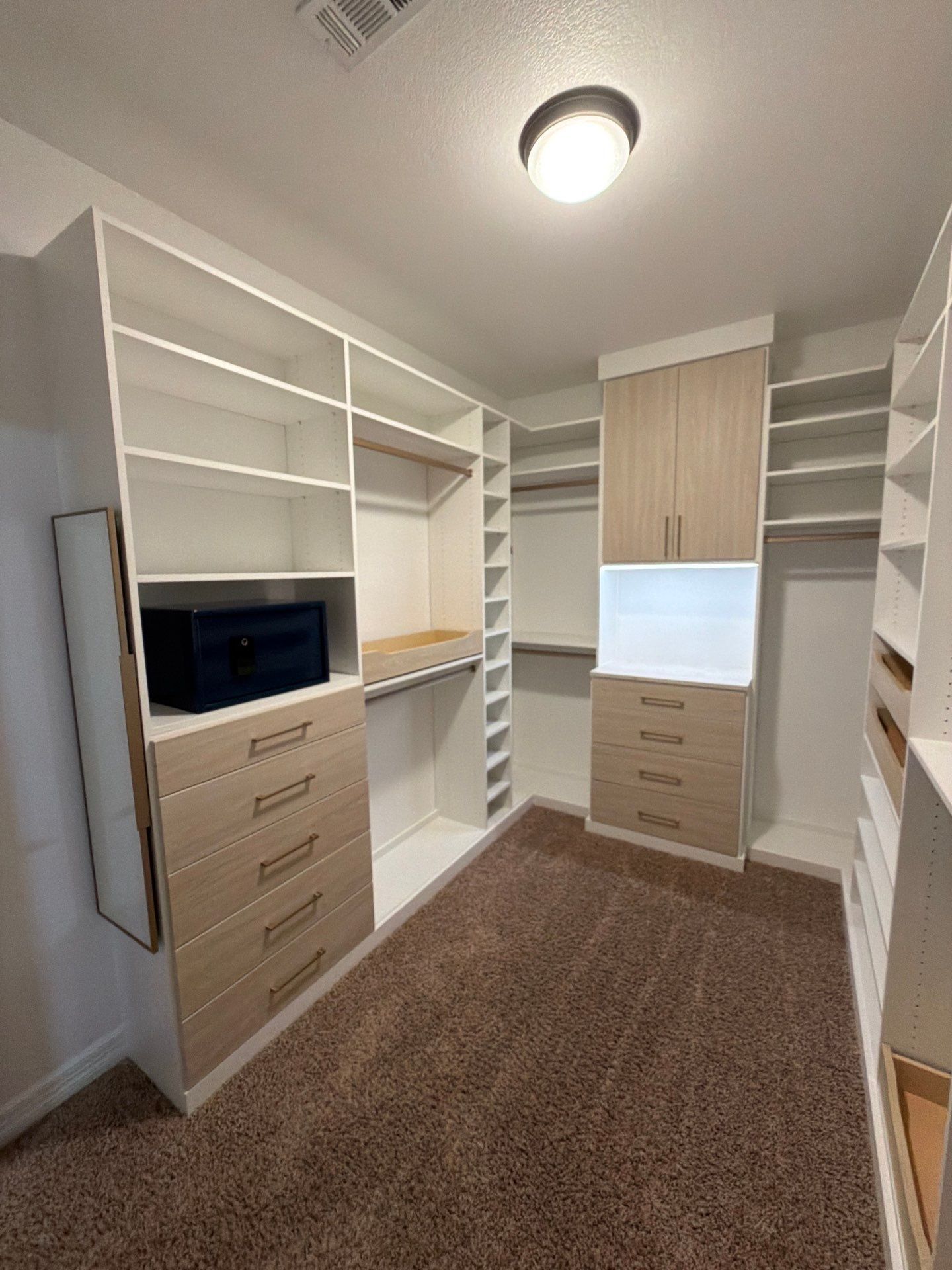Built-in walk-in closet with white shelves, drawers, and tan carpet under a ceiling light