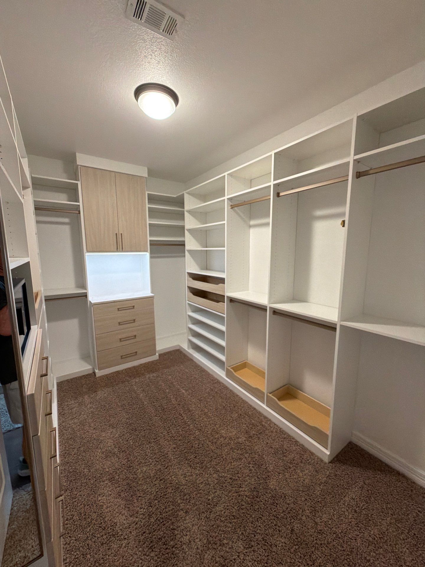 Walk-in closet with white shelving, drawers, hanging rods, and brown carpet flooring.