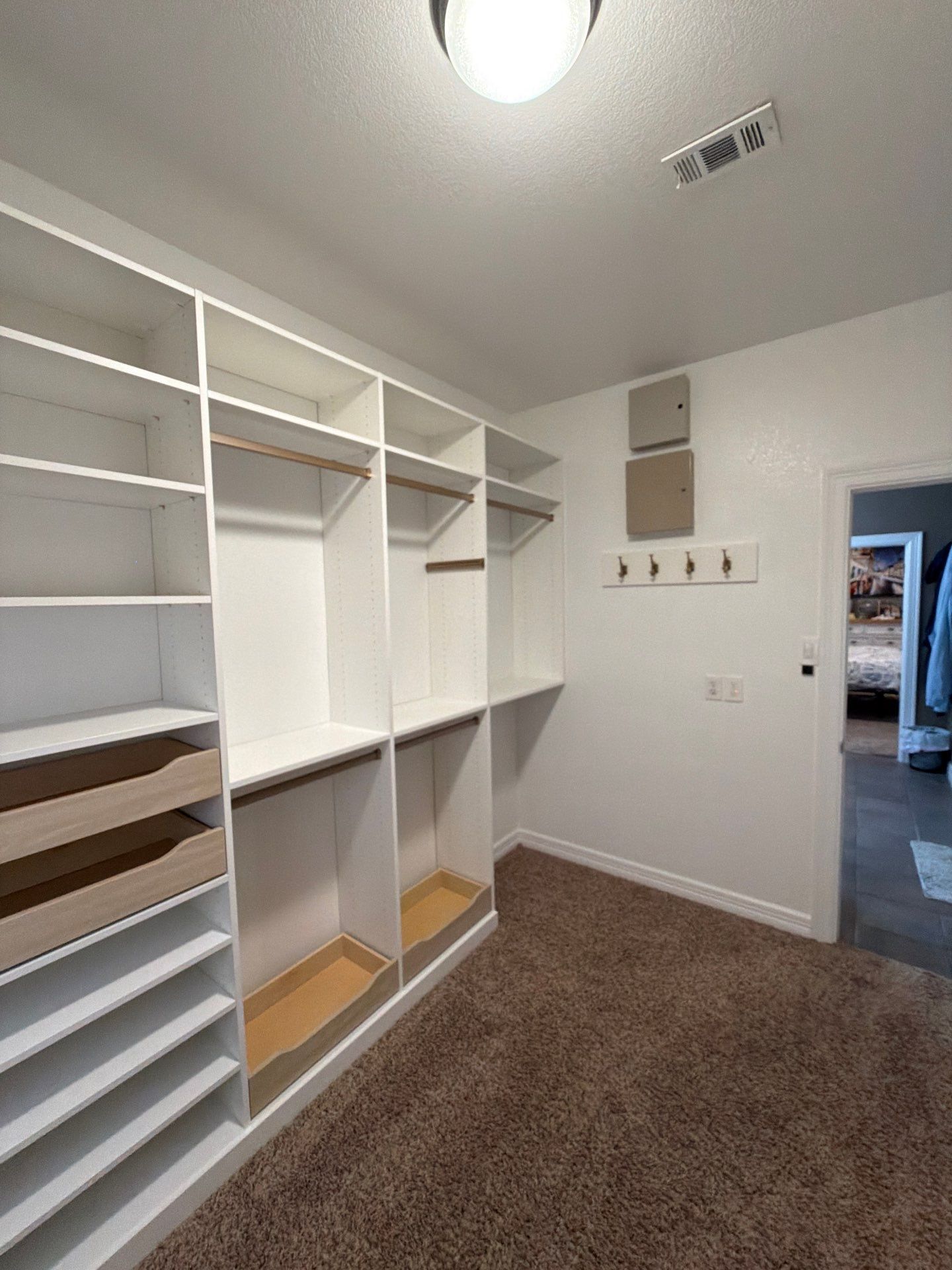 Empty walk-in closet with white shelving, hanging rods, and brown carpet.