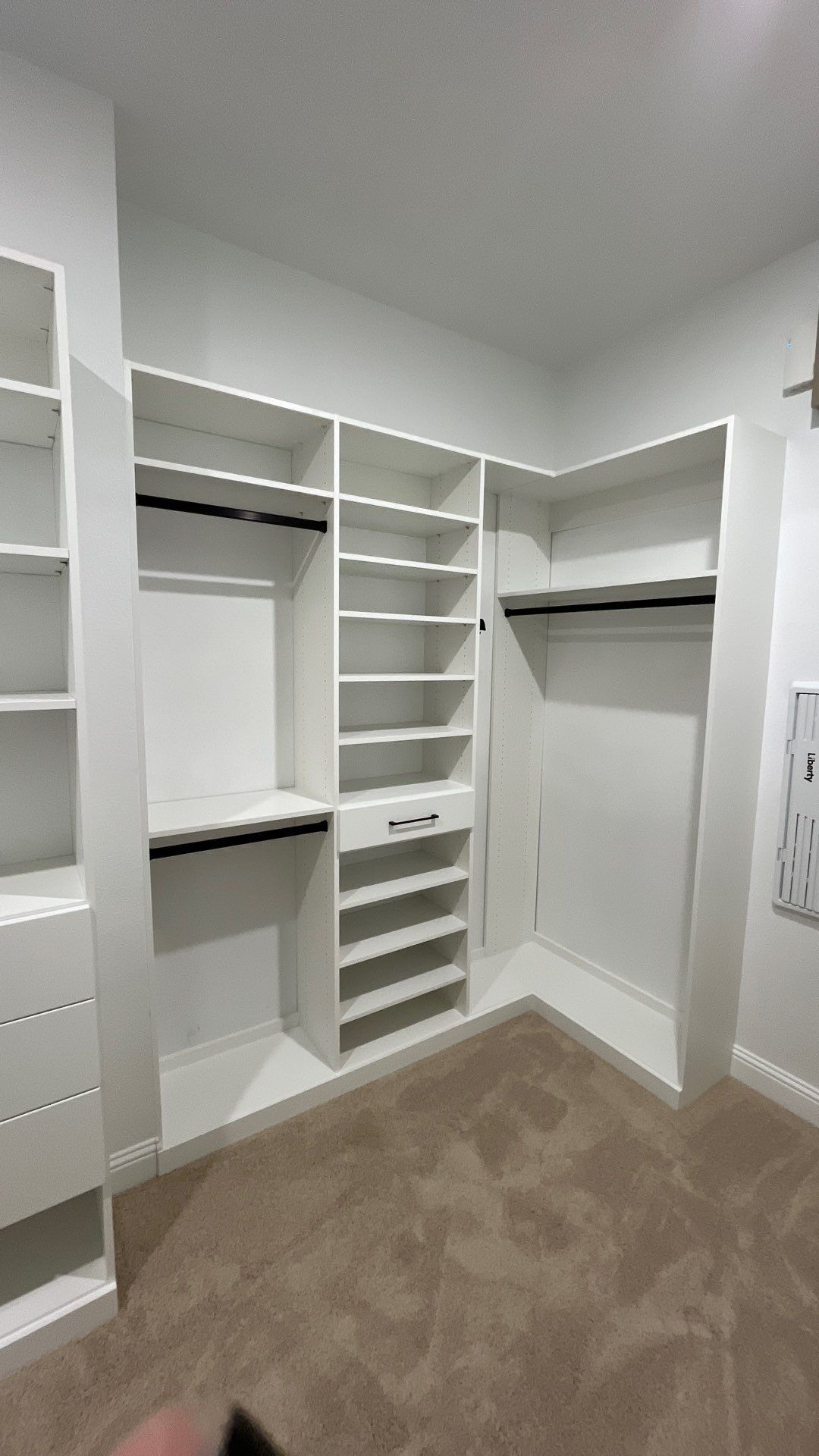 Walk-in closet with white shelving, hanging rods, drawers, and beige carpet.