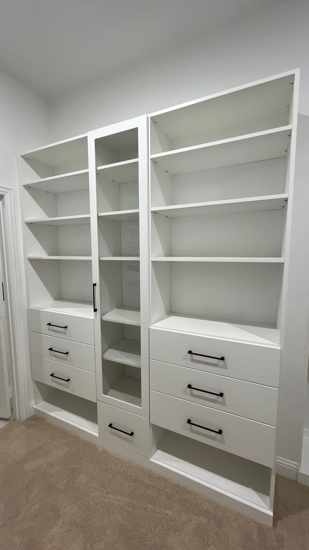White built-in closet shelves and drawers in a small room with beige carpet.