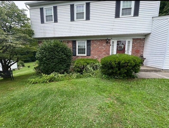 A white house with a brick wall and black shutters is sitting on top of a lush green hillside.