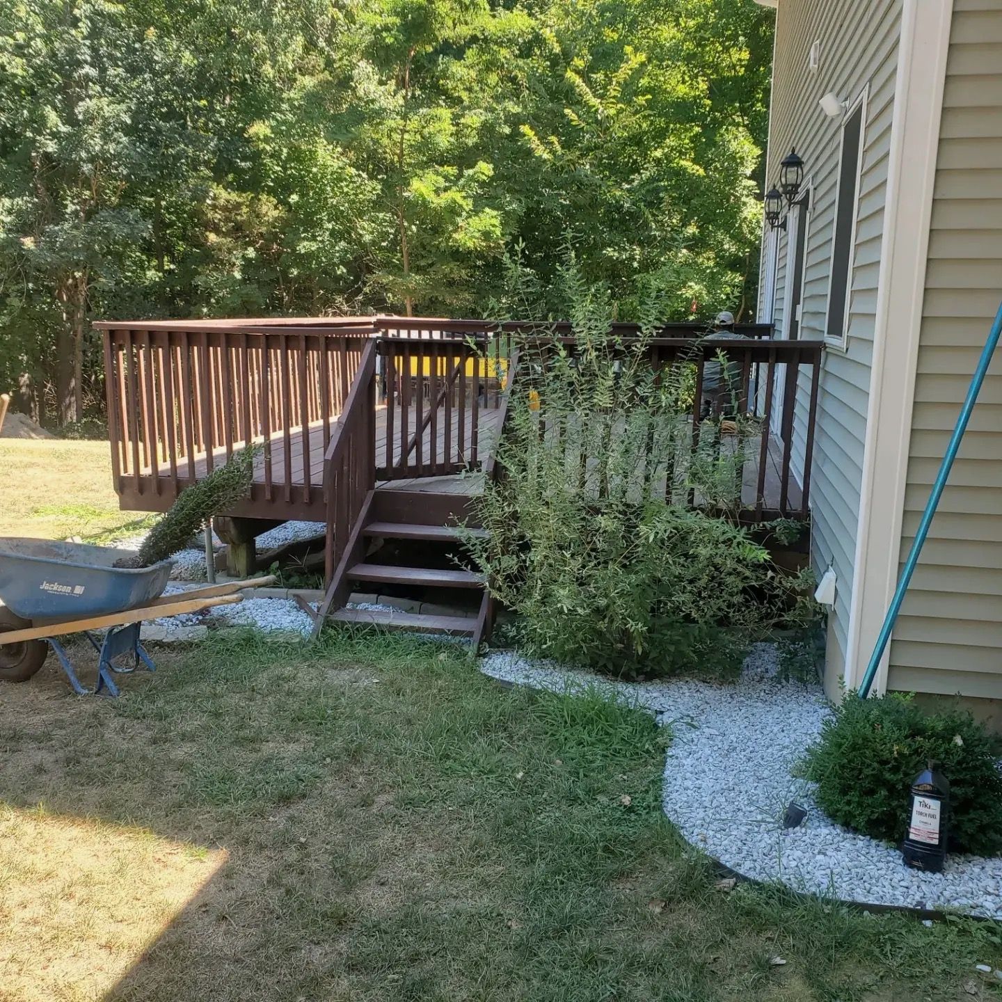 A wheelbarrow is parked in front of a house next to a deck.