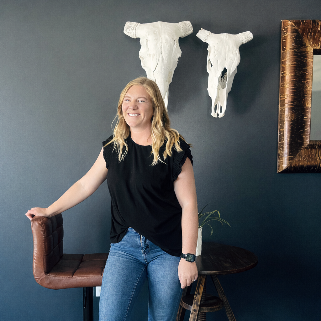 Smiling woman in black shirt and jeans leaning on a chair in a modern room with skull wall decor