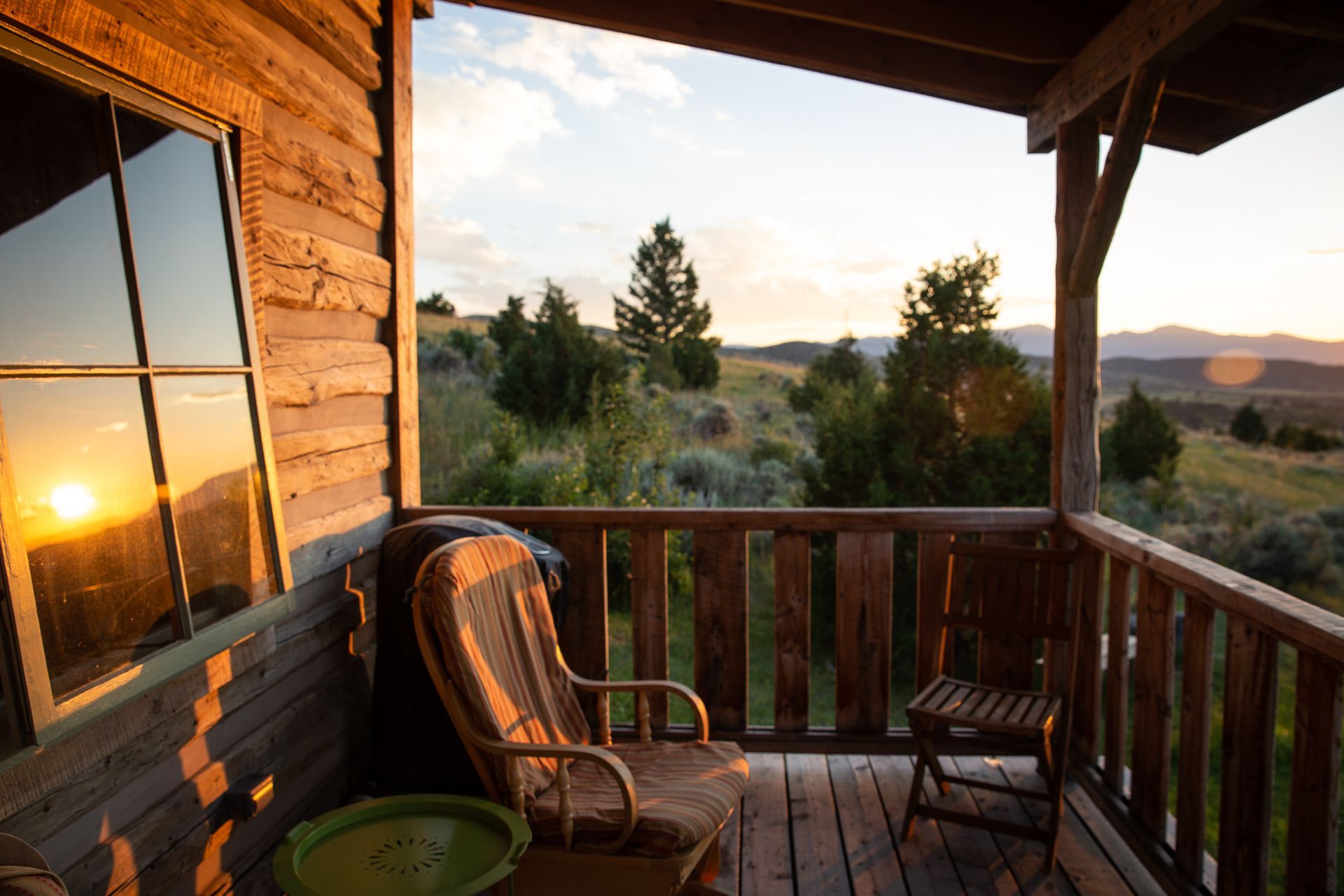 Sunset view from a rustic cabin porch with wooden chairs and a railing overlooking trees and hills
