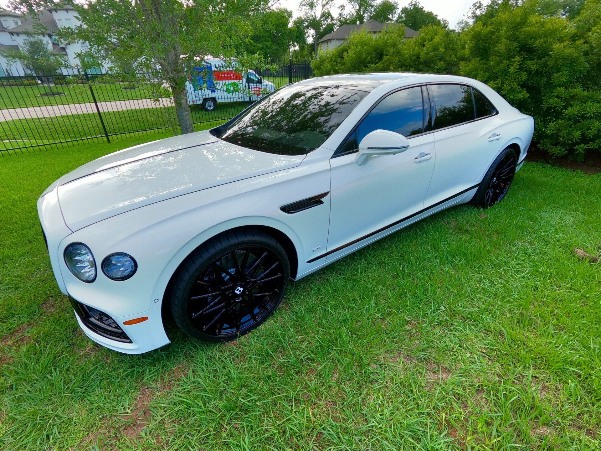 White Bentley sedan parked on green grass; black wheels and trim, tinted windows.