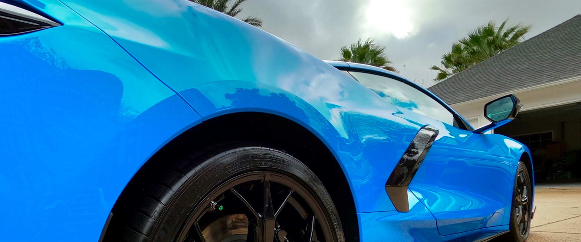 Blue sports car parked near a house under a cloudy sky.