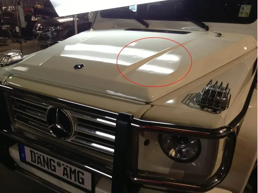 White Mercedes-Benz G-Class SUV with a prominent crease on the hood. A red circle highlights the creased area.