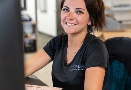 Woman smiles while looking at a computer; wearing a black shirt, indoor setting.