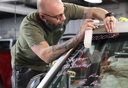 Man with tattoos sprays window of a vehicle with a spray bottle in a workshop.