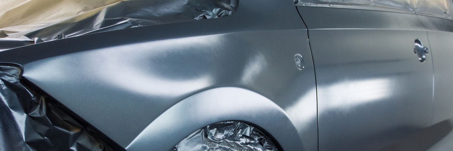 Silver car with a dented front side panel and crumpled hood after a crash