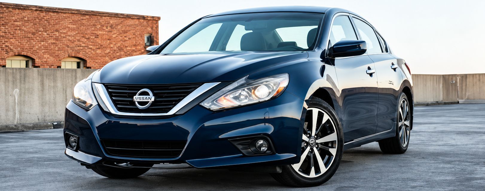 Blue Nissan sedan parked outdoors on pavement in front of a brick wall