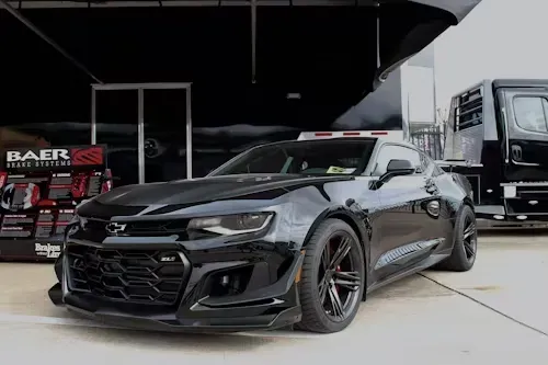 Black Chevrolet Camaro ZL1 sports car parked near a trailer, outdoors.