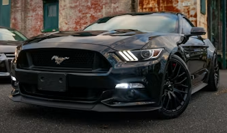 Black Ford Mustang parked on a street in front of a brick wall, front view