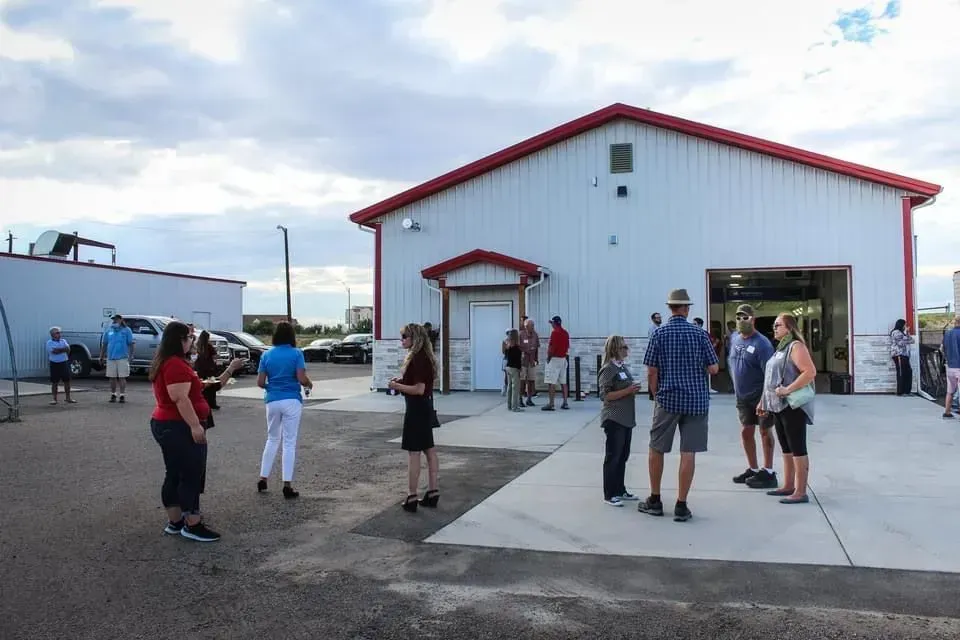 People gathered outside a white building with a red roof, cloudy sky.