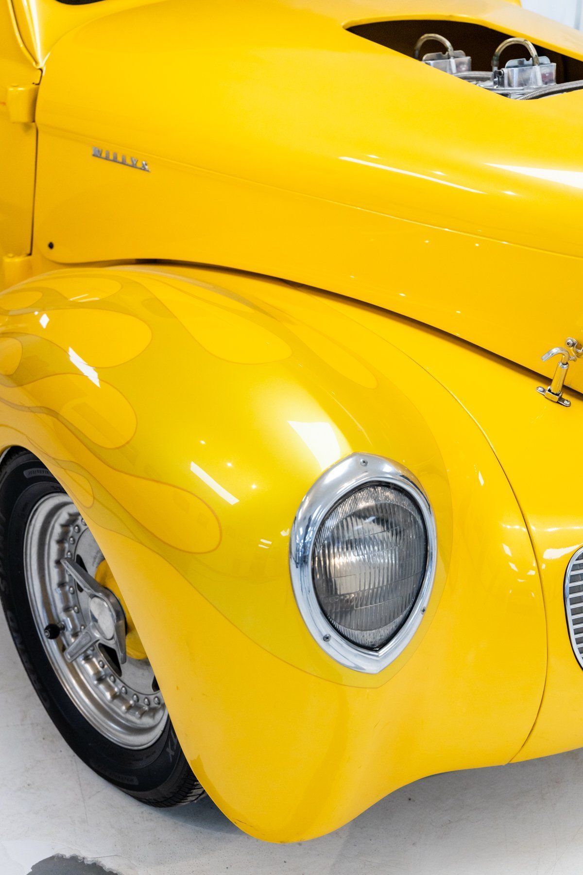 Yellow classic car with flame details on fender, chrome headlight, and open engine.