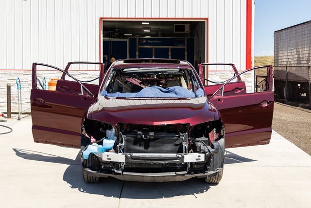 Maroon SUV with open doors and missing front components, parked in front of a building.